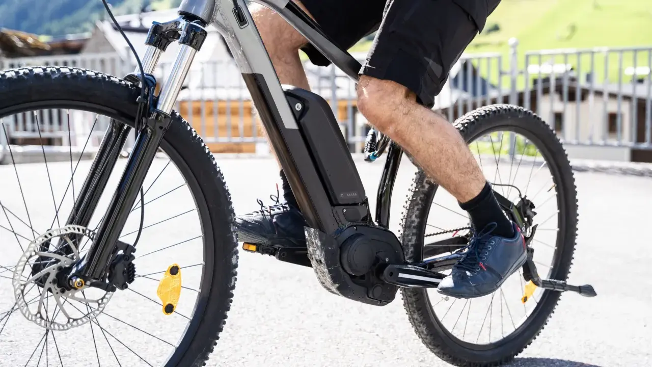 Mężczyzna pedałuje na rowerze elektrycznym, pokazując, jak działa rower elektryczny. Bateria i silnik są widoczne na ramie.