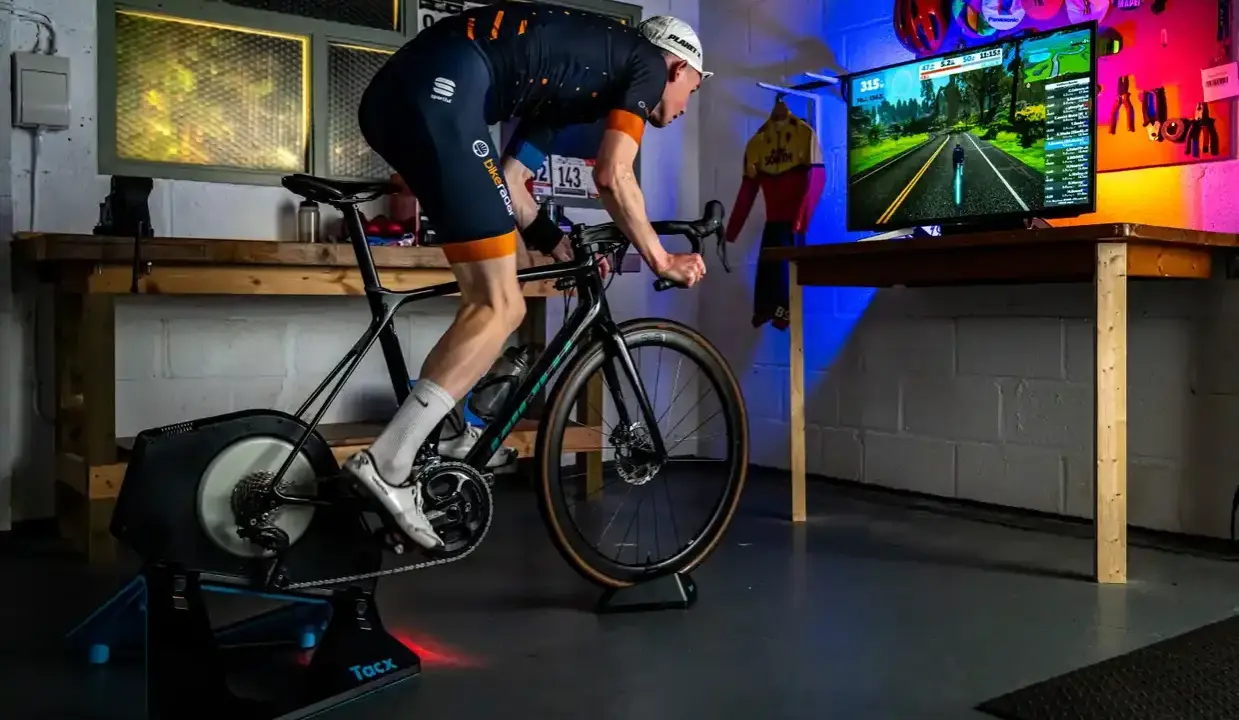 Intensywny trening na trenażerze kolarskim w wirtualnym świecie. Kolarz w stroju sportowym pedałuje, śledząc trasę na ekranie.