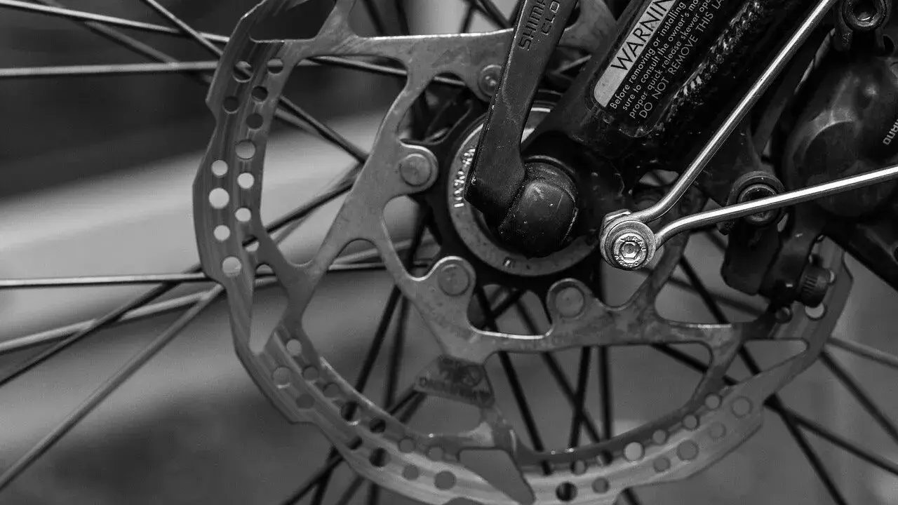 Zbliżenie na tarczę hamulcową i piastę roweru. Widać mechanizm przerzutki Shimano i ostrzeżenie na ramie.