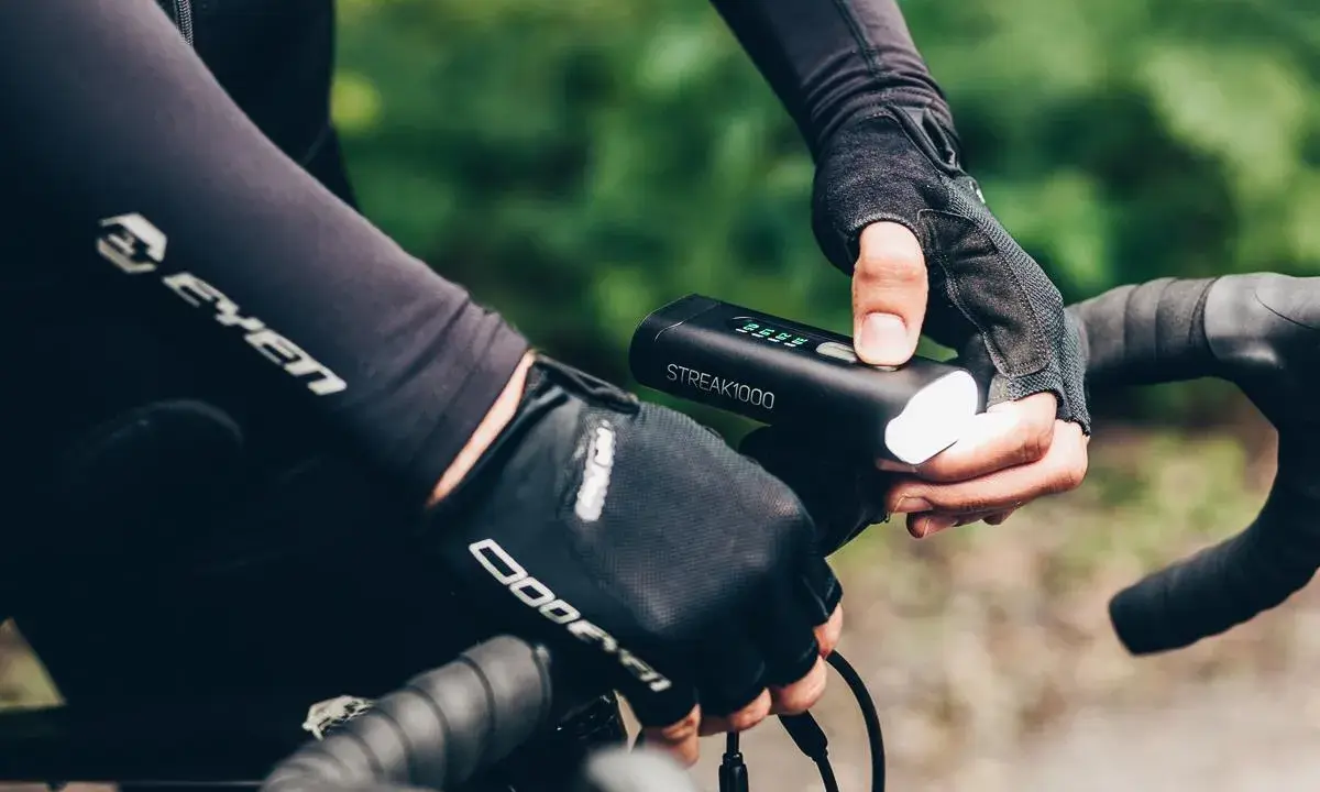 Rowerzysta w rękawiczkach sprawdza mocne oświetlenie rowerowe STREAK1000. Dobre oświetlenie to podstawa bezpieczeństwa.