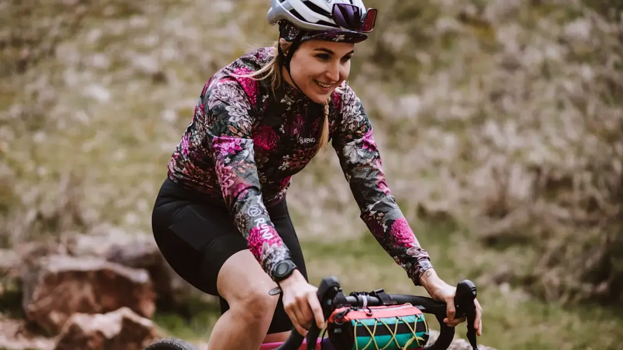 Uśmiechnięta rowerzystka w kwiecistej bluzie pokonuje kolejne kilometry. 100 km na rowerze to wyzwanie, ale radość z jazdy jest widoczna.