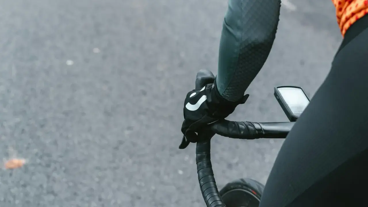 Rowerzysta w rękawiczkach z logo, trzymający kierownicę szosową. Kluczowe jest, jak dobrać szerokość kierownicy szosowej dla komfortu.