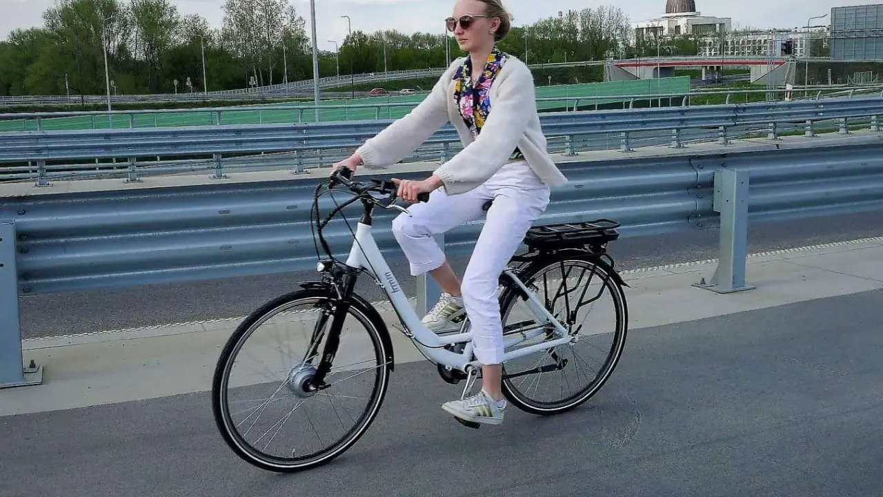 Kobieta na rowerze elektrycznym, ubrana na biało, jedzie po moście. Uważaj na przepisy, by nie dostać mandatu za rower elektryczny.
