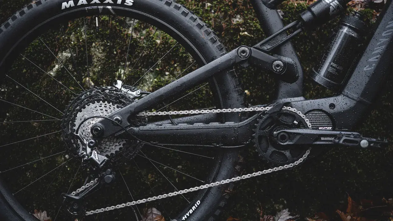 Część roweru elektrycznego z napędem **Shimano EP8** w deszczu. Widoczna kaseta, przerzutka, łańcuch i korba.