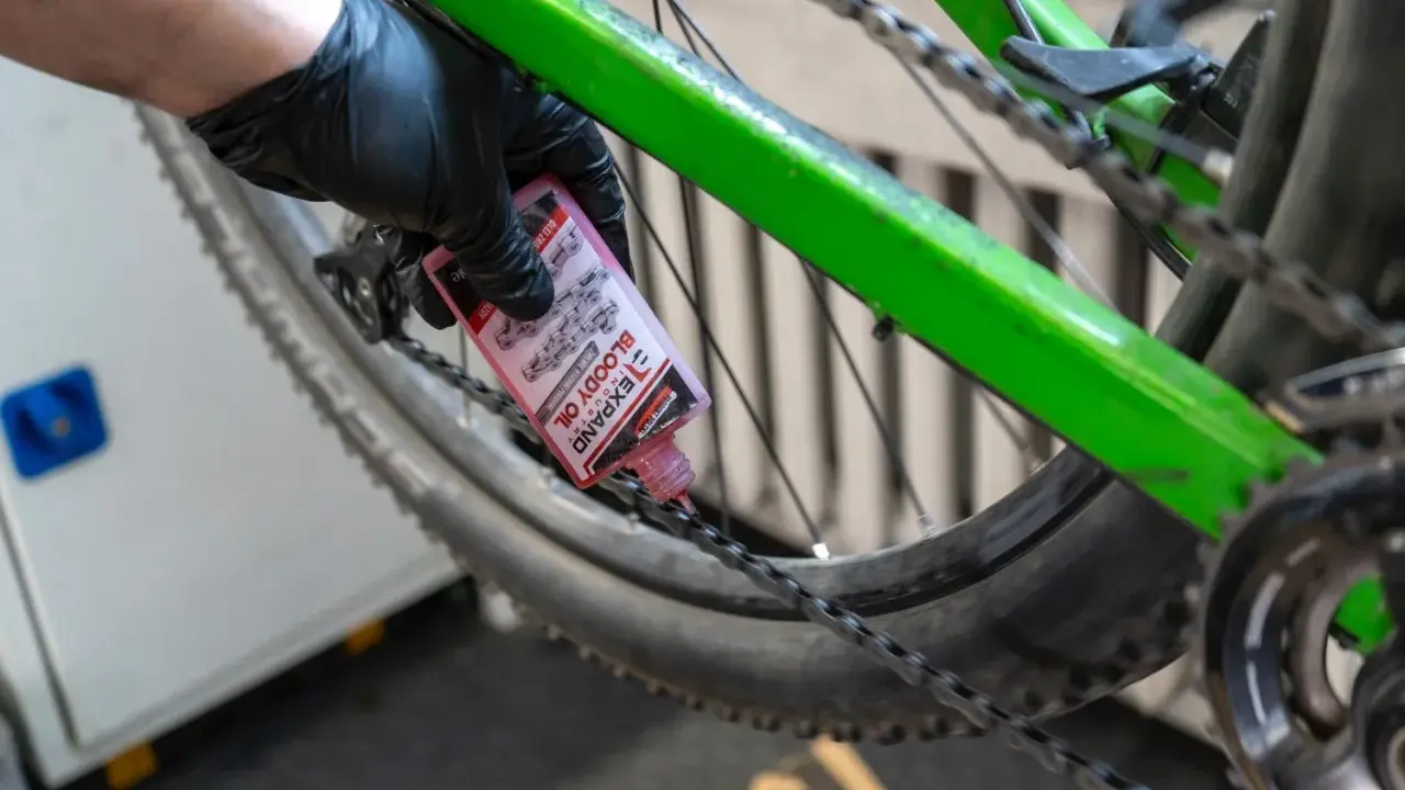Rękawiczka z czarną gumką aplikuje różowy olej do łańcucha roweru. To część przeglądu roweru, aby zapewnić płynną jazdę.