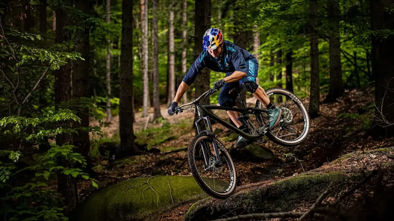 Kolarz w kasku Red Bull zjeżdża rowerem po leśnym stoku. To jest właśnie downhill – szybka jazda w dół!