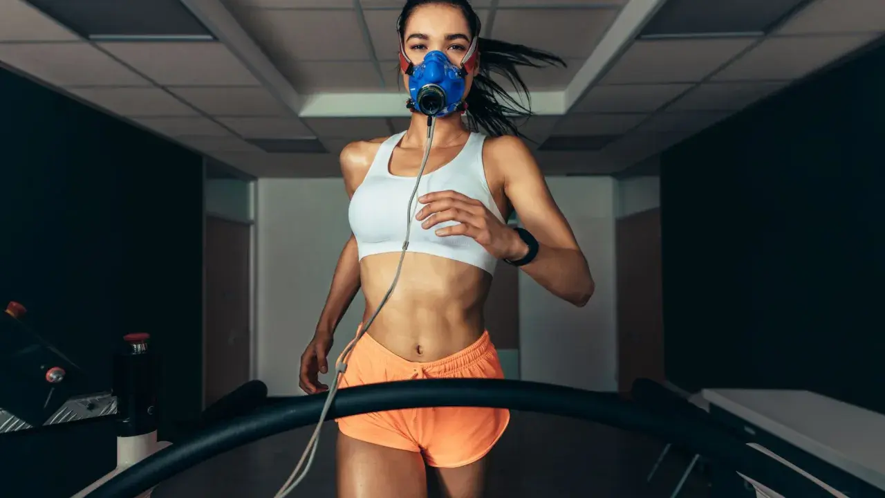 Kobieta w masce tlenowej biegnie na bieżni, badając swoje VO2max.