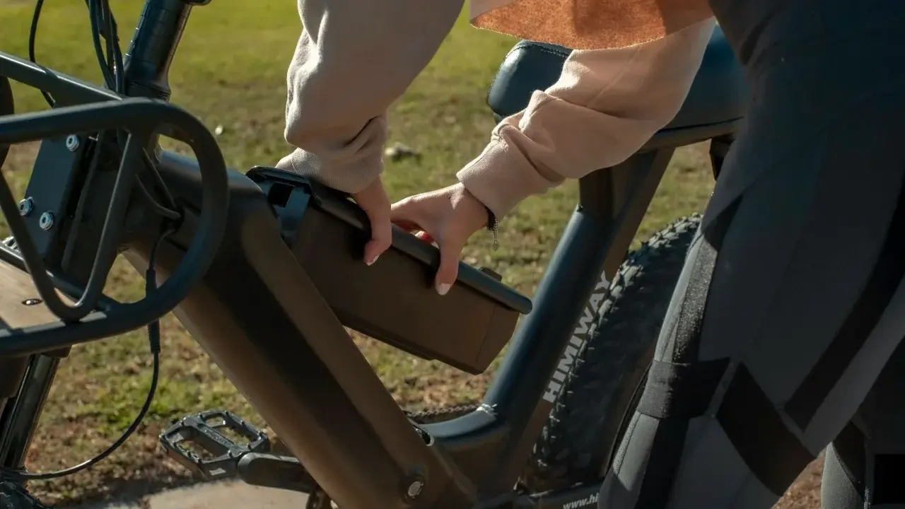Dłoń wyjmuje baterię z ramy roweru elektrycznego, pokazując, jak ładować rower elektryczny.