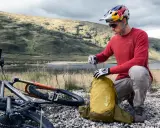 Rowerzysta w kasku przygotowuje żółty plecak Deuter. Idealny, jaki plecak na rower na górskie wyprawy.