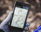 Rękawica trzyma smartfon z aplikacją **aplikacja trasy rowerowe** Trailforks, pokazującą mapę Beskidu Małego.