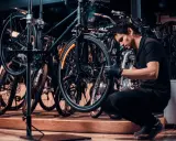 Mechanik w czarnej koszulce i rękawiczkach pokazuje, jak zdjąć tylne koło w rowerze, pracując w serwisie rowerowym.