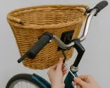 Instrukcja: jak zamontować koszyk do roweru click. Ręce dokręcają śrubę mocującą wiklinowy koszyk do kierownicy.