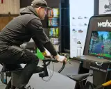 Mężczyzna na rowerze stacjonarnym z napędem **direct drive** wirtualnie przemierza trasę, widoczną na ekranie Wahoo.