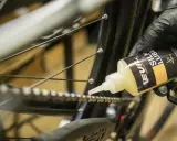 Rękawiczka z czarną rękawiczką aplikuje olej na łańcuch rowerowy, pokazując, jak nasmarować łańcuch w rowerze.