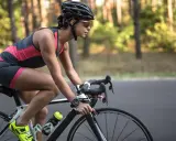 Kobieta w kasku i okularach przeciwsłonecznych pedałuje na rowerze szosowym przez las. Widać jej nogi w sportowym stroju i zegarek na ręce. To efekty po miesiącu regularnej jazdy na rowerze.