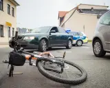 Wypadek drogowy: przewrócony rower, samochód i radiowóz policyjny. Maksymalne obciążenie roweru mogło przyczynić się do zdarzenia.