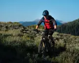 Kolarz MTB w kasku i czerwonej koszulce z plecakiem wodnym, jadący po górskim szlaku. Utrzymuje prawidłową pozycję na rowerze mtb, pochylony do przodu.