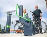 Stacja ładowania rowerów elektrycznych zasilana energią słoneczną. Para ludzi korzysta z nowoczesnych stojaków.