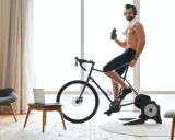 Mężczyzna w słuchawkach pije wodę, ćwicząc na rowerze stacjonarnym przy dobrej muzyce na rower.