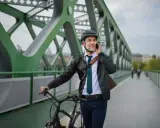 Mężczyzna w kasku i eleganckim stroju rozmawia przez telefon, prowadząc rower. Może to być jego nowy rower na firmę, idealny do miejskich dojazdów.