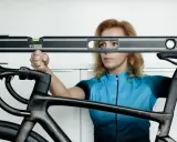 Kobieta w niebieskiej koszulce kolarskiej sprawdza poziom siodełka roweru szosowego.