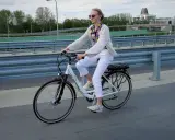 Kobieta na rowerze elektrycznym, ubrana na biało, jedzie po moście. Uważaj na przepisy, by nie dostać mandatu za rower elektryczny.