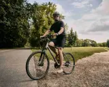 Mężczyzna w kasku i okularach jedzie na rowerze typu cross po leśnej ścieżce.