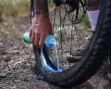 Ręka wylewa mleczko do opony rowerowej. To część przygotowania systemu **radial tubeless**, który zapewnia lepszą przyczepność i odporność na przebicia.