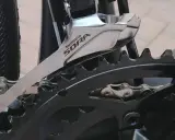 Montaż przedniej przerzutki Shimano Sora na rowerze. Widoczny fragment mechanizmu korbowego i łańcucha.