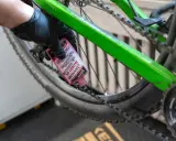 Rękawiczka z czarną gumką aplikuje różowy olej do łańcucha roweru. To część przeglądu roweru, aby zapewnić płynną jazdę.
