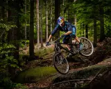 Kolarz w kasku Red Bull zjeżdża rowerem po leśnym stoku. To jest właśnie downhill – szybka jazda w dół!