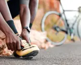 Rowerzysta zapina żółte buty, gotowy na kolejne wyzwania w **sporty rowerowe**. W tle widać rower.