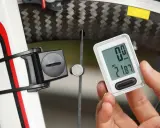 Dłoń trzyma licznik rowerowy, pokazując jak ustawić licznik rowerowy. Na ekranie widnieje dystans 21.87 km.