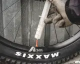 Rękawiczki i strzykawka z mleczkiem uszczelniającym przy wentylu koła rowerowego. Przygotowanie do **prostowania felg rowerowych** i uszczelnienia opony.