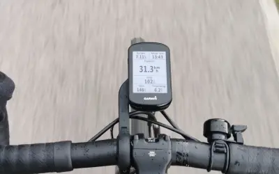 Na kierownicy roweru zamontowany jest licznik Garmin, który pokazuje dystans 7.11 km, tętno 146, rytm 102, temperaturę 6.2°C i aktualny czas 13:43. Prędkość 31.3 km/h jest widoczna na ekranie.