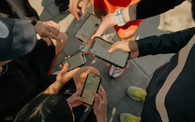 Grupa biegaczy analizuje swoje wyniki na telefonach. Widoczne ekrany aplikacji Strava po polsku pokazują mapy tras i statystyki.