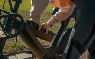 Dłoń wyjmuje baterię z ramy roweru elektrycznego, pokazując, jak ładować rower elektryczny.