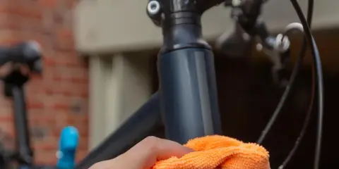 Dłoń z pomarańczową ściereczką czyści ramę roweru, przygotowując ją do wymiany sterów.