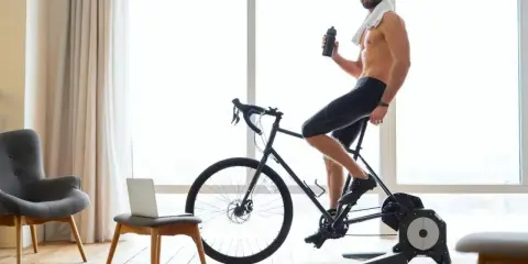 Mężczyzna w słuchawkach pije wodę, ćwicząc na rowerze stacjonarnym przy dobrej muzyce na rower.