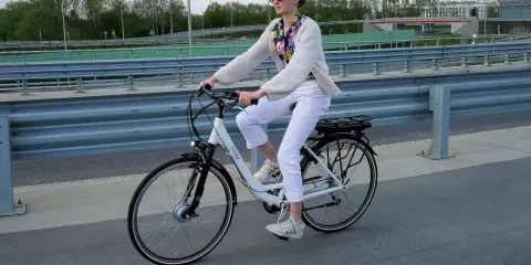 Kobieta na rowerze elektrycznym, ubrana na biało, jedzie po moście. Uważaj na przepisy, by nie dostać mandatu za rower elektryczny.