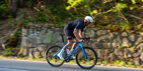 Kolarz w kasku ściga się na niebieskim rowerze Canyon Endurace CF 7 po malowniczej drodze wśród zieleni.