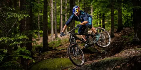 Kolarz w kasku Red Bull zjeżdża rowerem po leśnym stoku. To jest właśnie downhill – szybka jazda w dół!