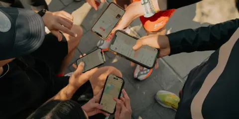 Grupa biegaczy analizuje swoje wyniki na telefonach. Widoczne ekrany aplikacji Strava po polsku pokazują mapy tras i statystyki.