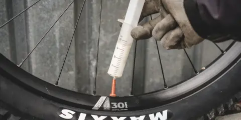 Rękawiczki i strzykawka z mleczkiem uszczelniającym przy wentylu koła rowerowego. Przygotowanie do **prostowania felg rowerowych** i uszczelnienia opony.