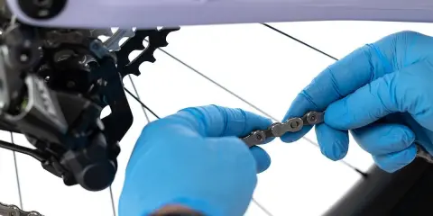 Ręce w niebieskich rękawiczkach dokonują wymiany łańcucha w rowerze, przygotowując go do kolejnej wyprawy.