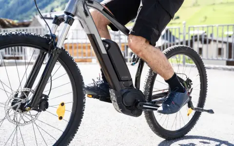 Mężczyzna pedałuje na rowerze elektrycznym, pokazując, jak działa rower elektryczny. Bateria i silnik są widoczne na ramie.