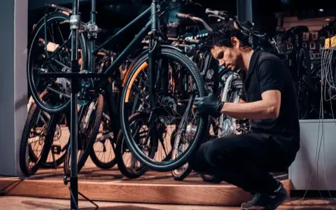 Mechanik w czarnej koszulce i rękawiczkach pokazuje, jak zdjąć tylne koło w rowerze, pracując w serwisie rowerowym.