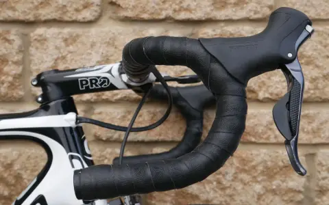 Czarna, wzorzysta owijka na kierownicę roweru szosowego z czarnymi manetkami Shimano.