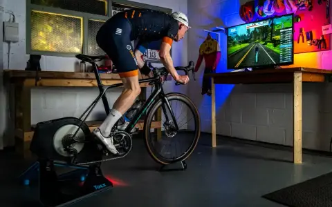 Intensywny trening na trenażerze kolarskim w wirtualnym świecie. Kolarz w stroju sportowym pedałuje, śledząc trasę na ekranie.