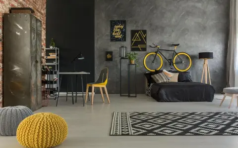 Kreatywne rozwiązanie, gdzie trzymać rower w bloku: zawieszony nad łóżkiem. Styl industrialny, czarno-żółta kolorystyka.